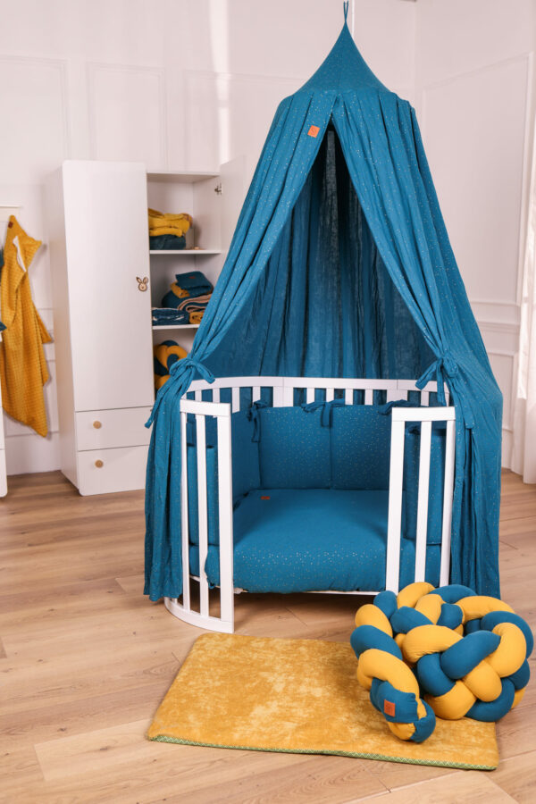 Lettino montessori Venere con baldacchino e completo piumone e paracolpi in mussola Shiny ottanio, treccia in mussola senape su tappeto giochi termico, con armadio per neonato sullo sfondo